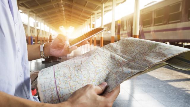 Traveler holding map, waiting for a train at train station and planing for next trip by mobilephone.Vintage tone, Retro filter effect, Soft focus, Low light.(selective focus)
